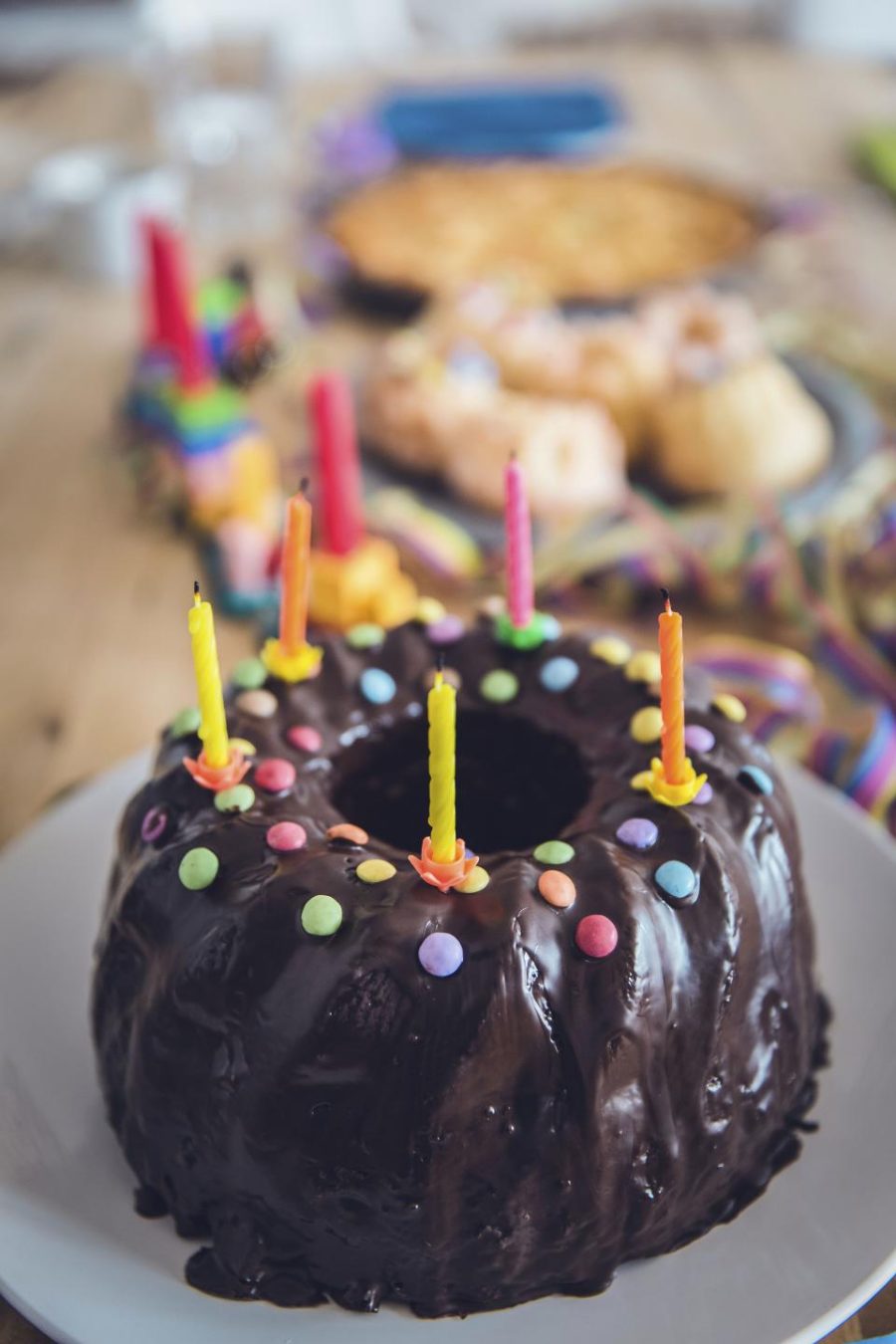 A chocolate birthday cake crowded with lit rainbow candles.