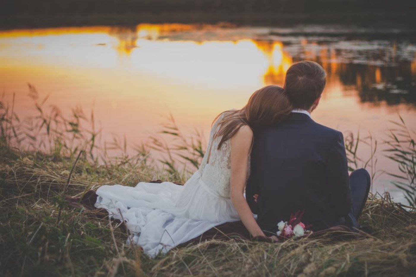 A photographer's shot: the couple seated together at the edge of a golden lake.